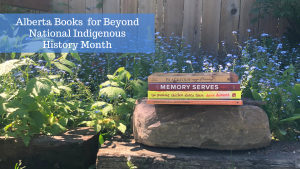 Alberta Books for Beyond National Indigenous History Month: A stack of four books on a rock. Blue flowers and greenery is in the background.